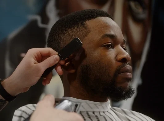 White guy doing a haircut to a young joyful african american guy in a beautiful barbershop