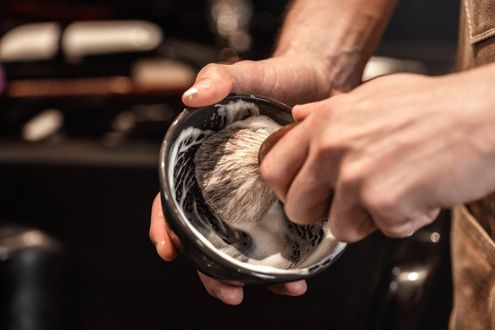hands of barber with brush for shaving beard and bowl
