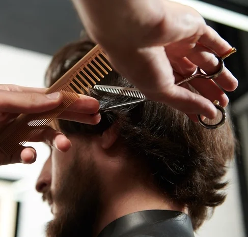 Brunet man getting haircut by a hairdresser while sitting in a chair at barbershop.