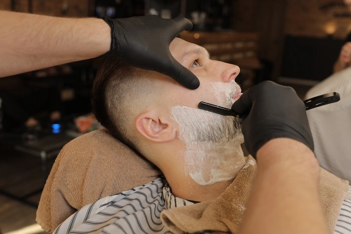 Barber Man is shaving client with a vintage straight razor in a barbershop