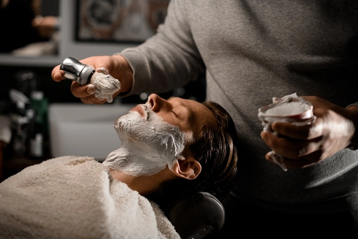 Hairdresser applying shaving foam on client's beard