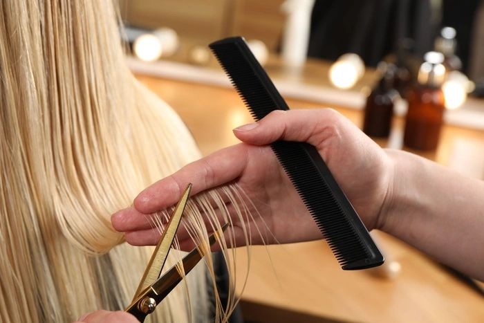 Hairdresser cutting client's hair with scissors in salon, closeup