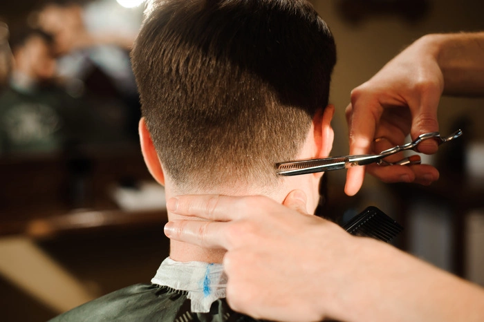 Master cuts hair and beard of men in the barbershop, hairdresser makes hairstyle for a young man